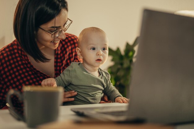 Mooie zakelijke moeder die een laptop gebruikt en thuis tijd doorbrengt met haar zoontje