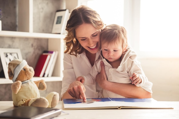 Mooie zakelijke moeder in pak leest een boek met haar schattige babyjongen en lacht thuis