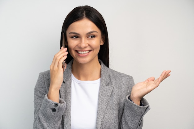 Mooie zakenvrouw die aan de telefoon praat en glimlacht, aangenaam gesprek met zakenpartner, afspraak maken. Indoor studio-opname geïsoleerd op een witte achtergrond