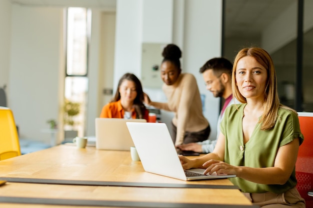 Foto mooie zakenvrouw die aan een laptop werkt met haar jonge multi-etnische startupteam in het moderne kantoor