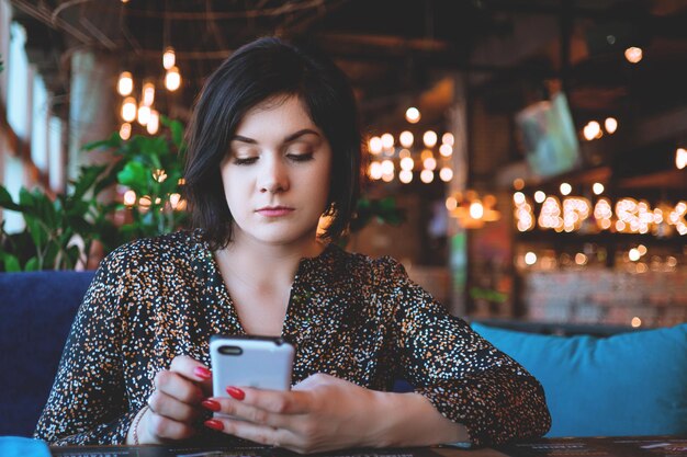 Mooie zakenvrouw in het restaurant belt op je smartphone Schattige brunette in een café