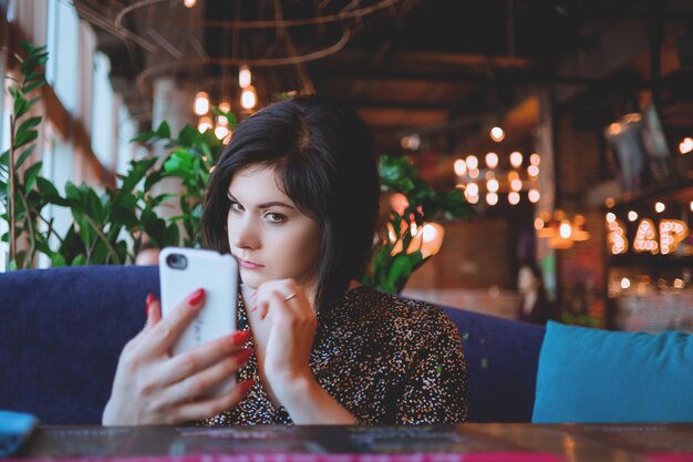 Mooie zakenvrouw in het restaurant belt op je smartphone Schattige brunette in een café