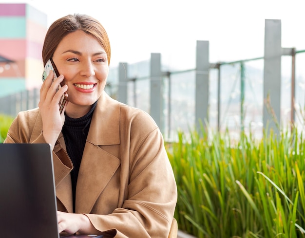 Foto mooie zakenvrouw op laptop en telefoon glimlachend kopie ruimte vegetatie achtergrond