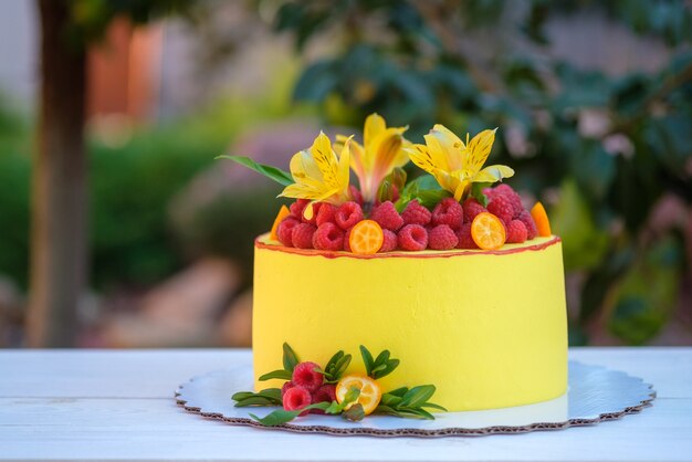 Mooie zelfgemaakte cake met felgele glazuur, versierd met levende lelies en verse frambozen