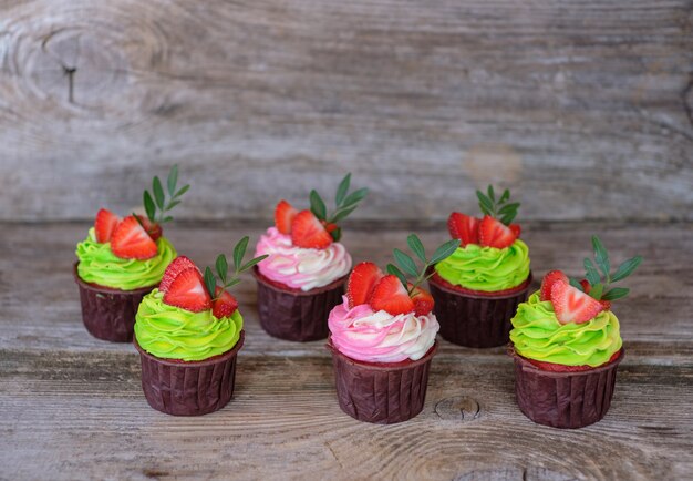 Foto mooie zelfgemaakte cupcakes met veelkleurige kaascrème, versierd met aardbeien, op een houten tafel