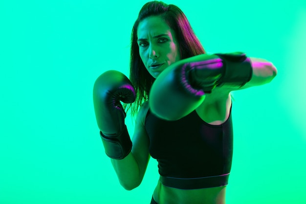 Mooie zelfverzekerde jonge fitness meisje staande geïsoleerd over groene neon muur, boksen