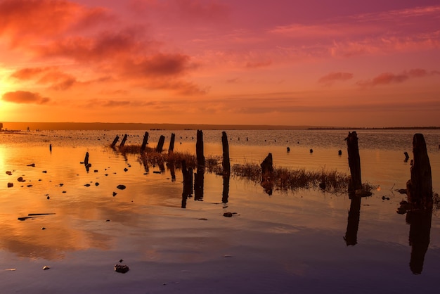 Mooie zonnige rode kleurrijke zonsondergang op het meer met stenen houten palen en reflectie natuurlijke seizoensgebonden zomervakantie achtergrond