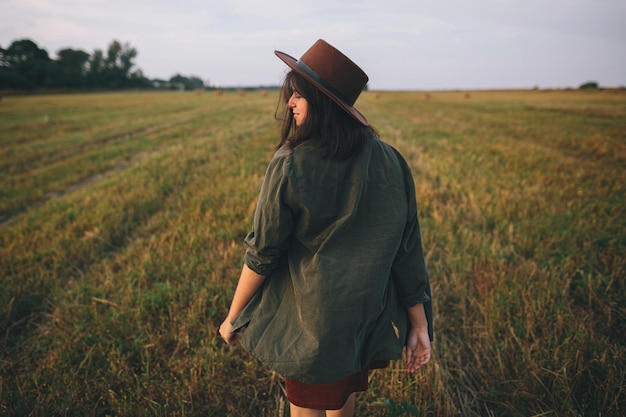 Mooie zorgeloze vrouw met hoed wandelen en glimlachen in de avond zomer veld Ontspannen op het platteland