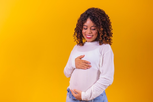 Mooie zwangere afro-vrouw op gele achtergrond met vrije ruimte voor tekst