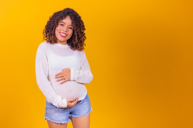 Mooie zwangere afro-vrouw op gele achtergrond met vrije ruimte voor tekst