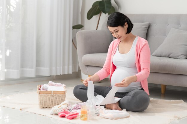 Mooie zwangere aziatische vrouw die een penschrijflijst gebruikt voor het inpakken van een notebook en het voorbereiden van babykleding in de mand