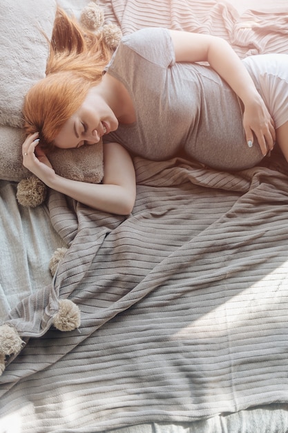 Mooie zwangere vrouw die bij bed het rusten leggen