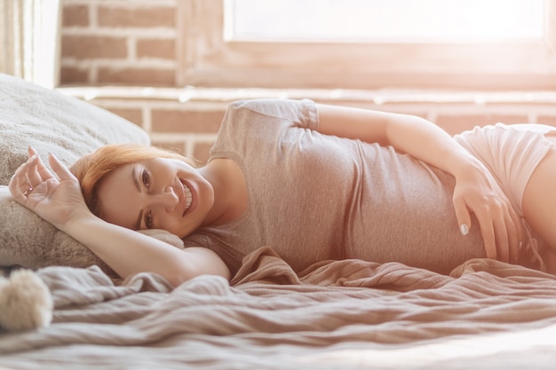 Mooie zwangere vrouw die bij bed het rusten leggen