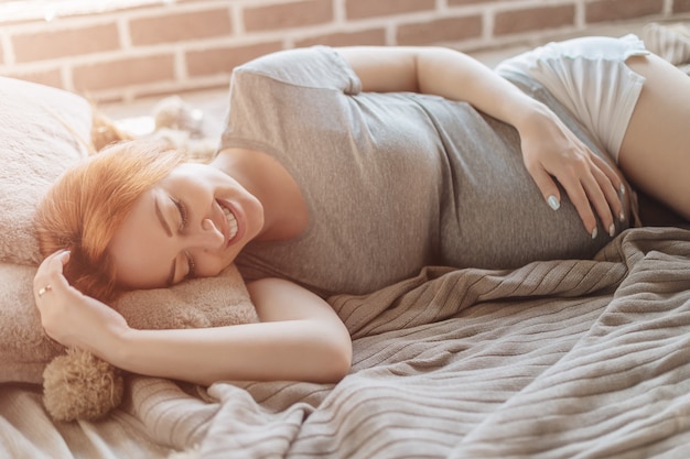 Mooie zwangere vrouw die bij bed het rusten leggen