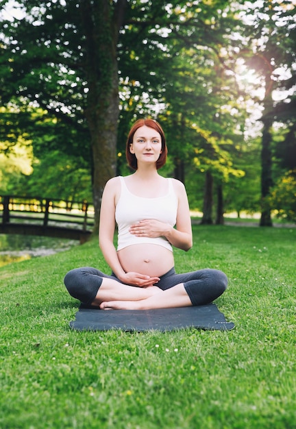 Mooie zwangere vrouw die prenatale yoga doet op de natuur buitenshuis