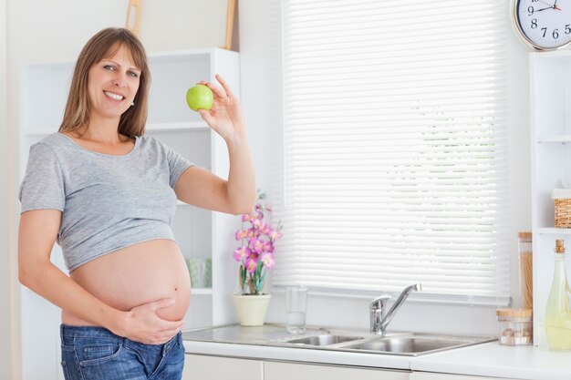 Mooie zwangere vrouw die terwijl het houden van een groene appel stelt