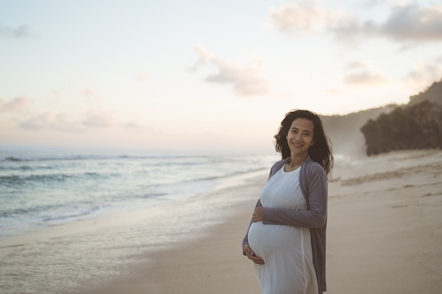 Mooie zwangere vrouw die zich op het strand bevindt