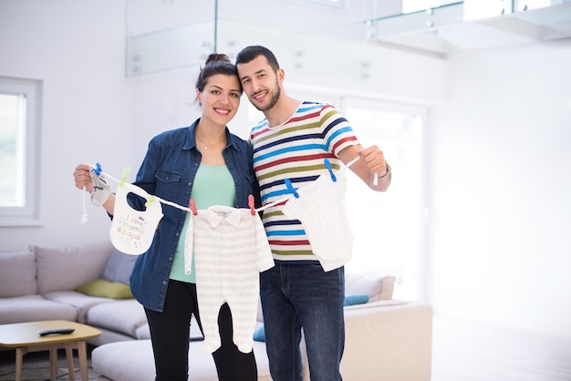 Mooie zwangere vrouw en haar man verwachten een baby met baby bodysuits en glimlachen thuis