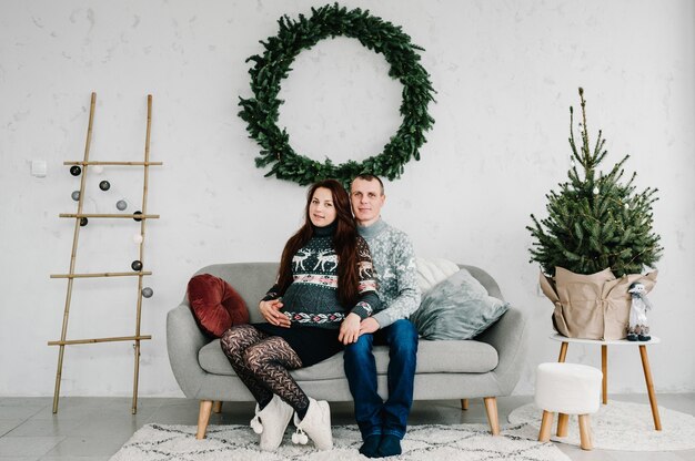 Mooie zwangere vrouw en man in zachte truien op de bank in de buurt van de boom