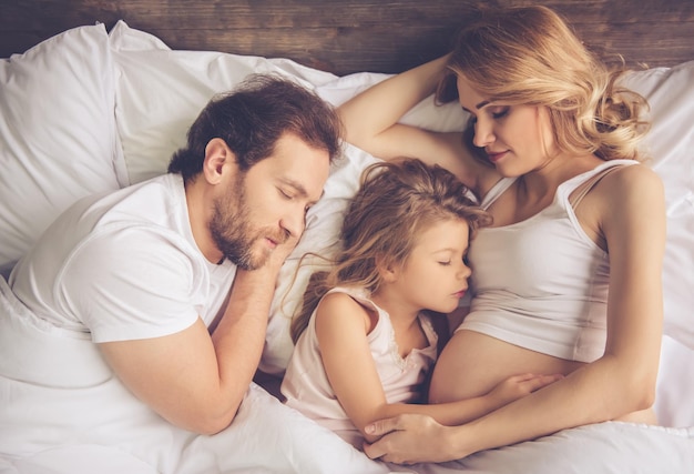 Mooie zwangere vrouw, haar knappe echtgenoot en schattig dochtertje slapen samen in bed