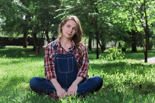 Mooie zwangere vrouw in denim overalls zittend op het gras in het park