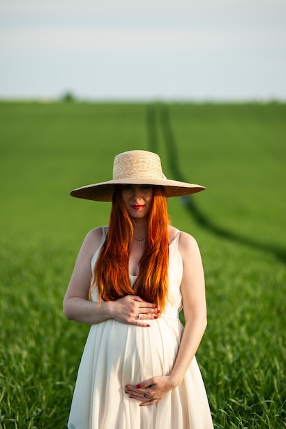 Mooie zwangere vrouw in witte jurk wandelen in het groene veld