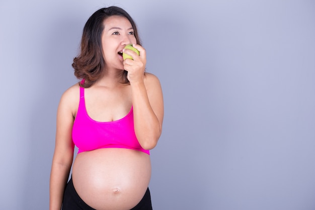 Mooie zwangere vrouw met appel op grijze achtergrond