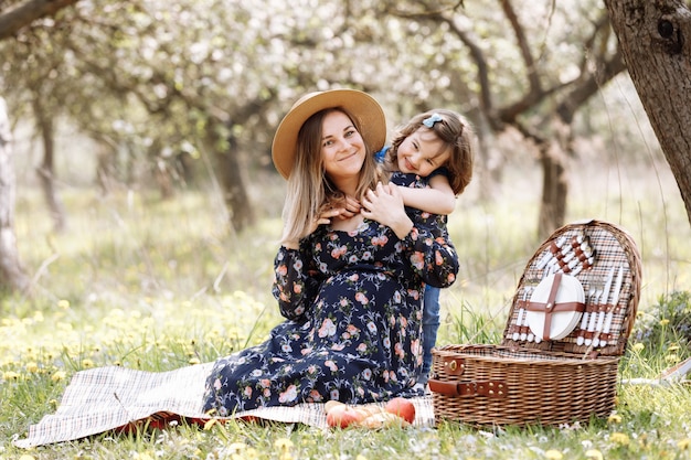 Foto mooie zwangere vrouw met dochtertje spelen op een picknick in een bloeiende lentetuin