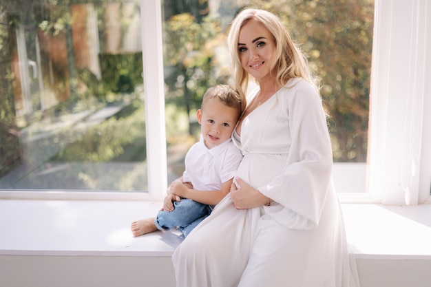 Mooie zwangere vrouw met haar zoon jongen knuffelt zijn moeder en verheugt zich jongen die wacht op zusterdame in