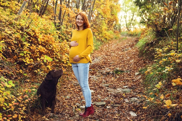 Mooie zwangere vrouw op een wandeling met de hond in de herfst. Zwangerschap en huisdieren.