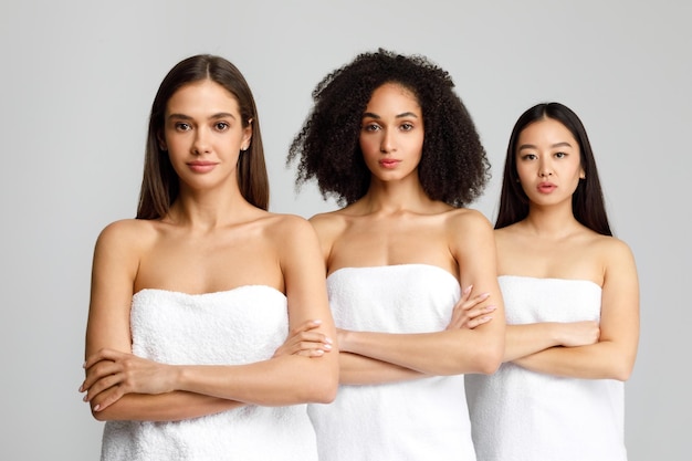 Mooie zwarte blanke en Aziatische vrouwen poseren met gevouwen armen in badhanddoeken en staan in de rij.