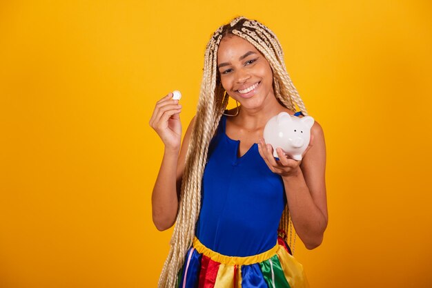 Mooie zwarte braziliaanse vrouw met vlechten die kleding dragen voor carnaval Holding munt en spaarvarken