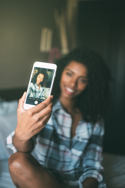 Mooie zwarte die een selfie bij bed het glimlachen maakt