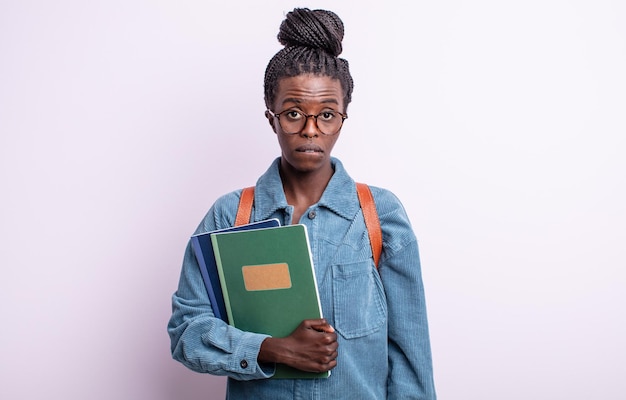 Mooie zwarte vrouw die verbaasd en verward kijkt. student met boeken concept