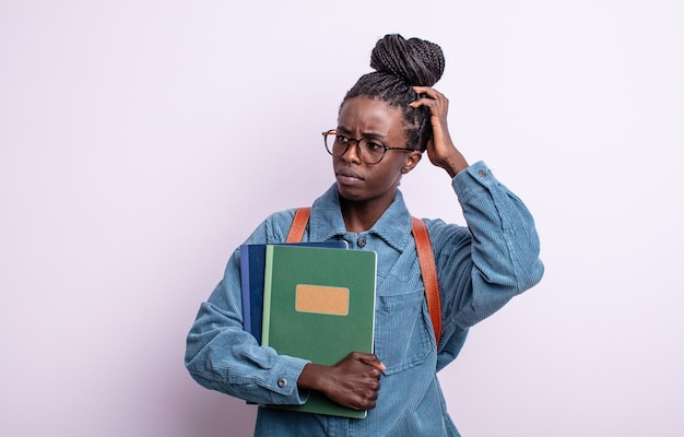 Mooie zwarte vrouw die zich verward en verward voelt, hoofd krabben. student met boeken concept