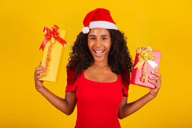 Mooie zwarte vrouw in Kerstman hoed met vrolijk kerstcadeau op gele achtergrond.