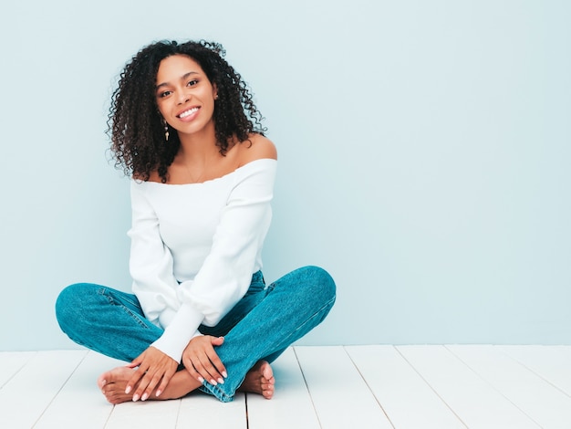 Mooie zwarte vrouw met afro krullen kapsel. Glimlachend model in trui en trendy jeanskleding