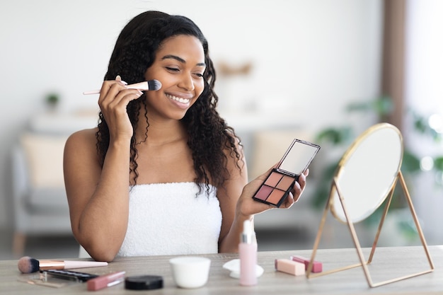 Mooie zwarte vrouw met contourpalet die make-up zet