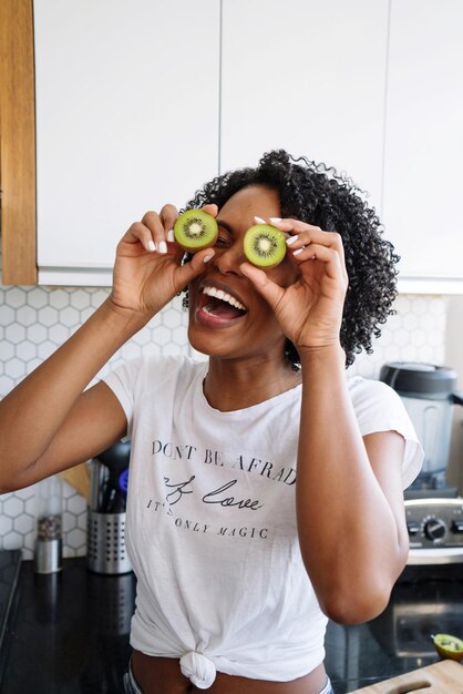 Mooie zwarte vrouw met krullend haar met kiwi's in haar handen.