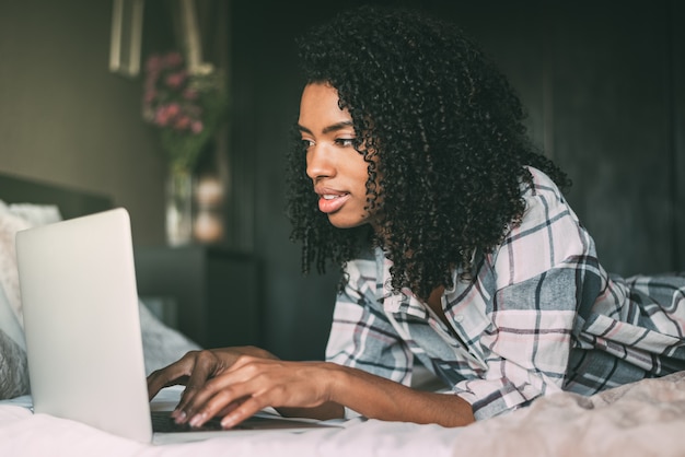 Mooie zwarte vrouw op bed met laptop en kopje koffie