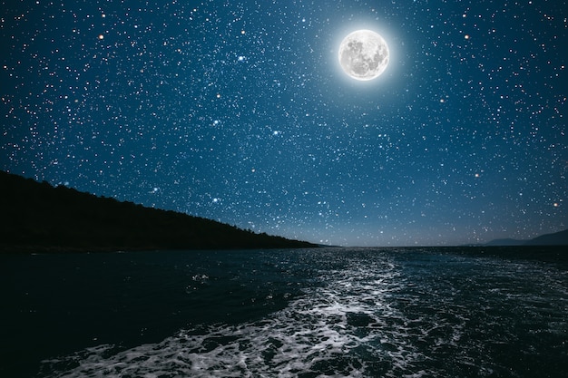 밝은 밤 별이 빛나는 하늘을 배경으로 달이 바다에 반사되었습니다.