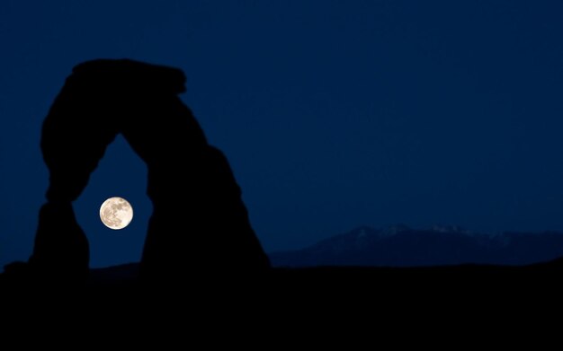 Photo a moon is shining in the night sky behind a large rock