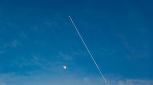空に煙の道がある月と飛行機