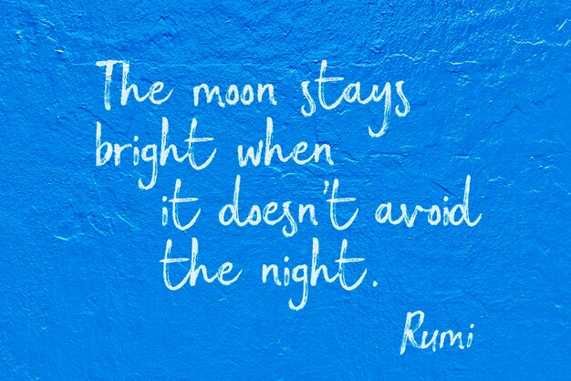 The moon stays bright when it doesnt avoid the night  ancient Persian poet and philosopher Rumi quote handwritten on blue wall