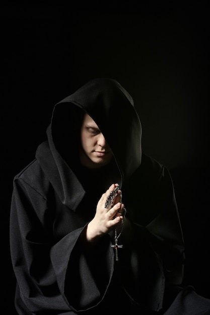 Moordenaar in donkere kleren in de kerk. Tovenaar in zwarte mantel die mysterieuze ritus in donkere kamer doet. Monnik bidt in het donker. Magisch ritueel in de schaduw. Sinner in zwarte kap heeft berouw in schaduw. Mystery man.