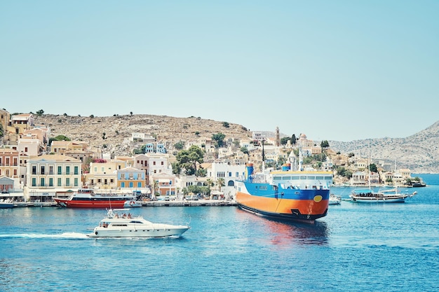 Moored cruise ferry on sea against town with old multicolored buildings on hills on Symi island