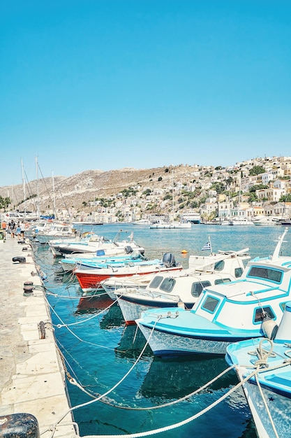 Moored motorboats on azure sea against historical tourist city in Greece on Symi island