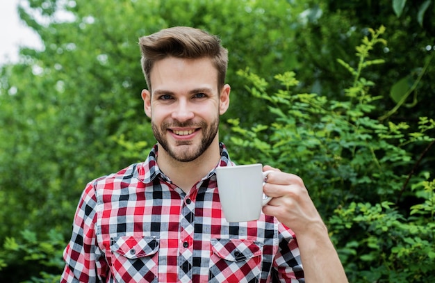 Еще кофе красивый бородатый парень пьет чай на открытом воздухе он любит какао еду и напитки веселый мужчина в клетчатой рубашке пьет утренний кофе доброе утро свежее вдохновение и энергичный напиток