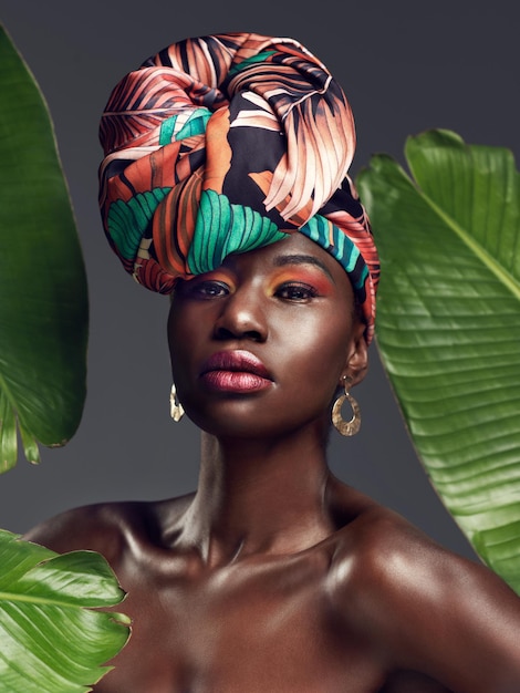 단순히 내 왕관을 천으로 만드는 것 이상으로, 녹음이 우거진 배경에 대해 전통적인 아프리카 머리 랩을 쓰고 있는 아름다운 젊은 여성의 스튜디오 샷
