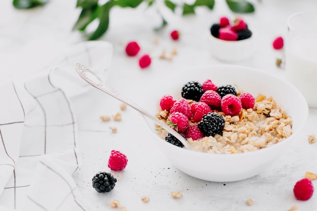 Morgen gezond ontbijt witte kom vol met granola muesli raspberry zwarte bessen op grijze tafel